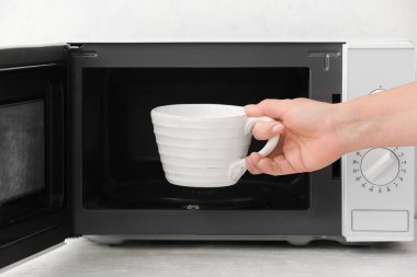 Mikrodalga fırından sütlü fincan alan kadın, yakın plan.