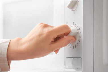 Genç bir kadın mikrodalga fırında yemek ısıtıyor.