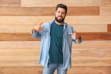 Yakışıklı adam ahşap arka plandaki mavi tişörtü işaret ediyor.