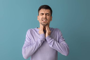 Mavi arka planda boğazı ağrıyan genç bir adam.