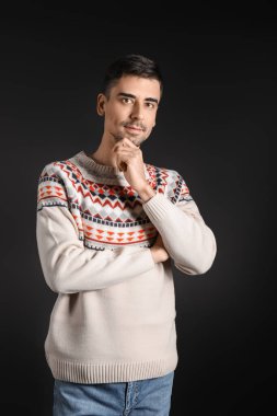 Esmer arka planda örülü süveter giyen yakışıklı bir genç.