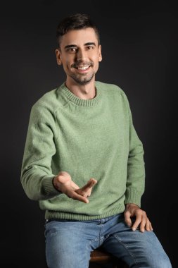 Esmer arka planda örülü süveter giyen yakışıklı bir genç.