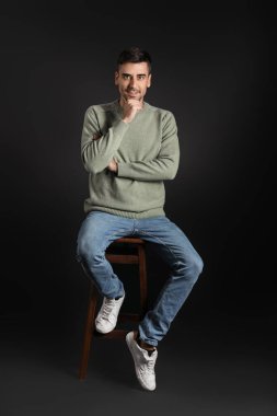 Esmer arka planda örülü süveter giyen yakışıklı bir genç.