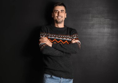 Esmer arka planda örülü süveter giyen yakışıklı bir genç.