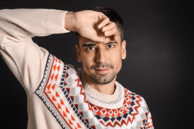 Esmer arka planda örülü süveter giyen yakışıklı bir genç.