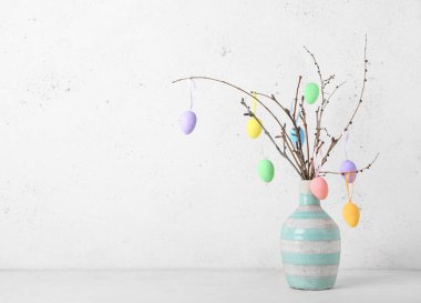 Ağaç dallı vazo ve arka planda farklı Paskalya yumurtaları.