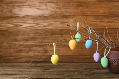 Ağaç dallı kil vazo ve ahşap arka planda farklı Paskalya yumurtaları, yakın plan.
