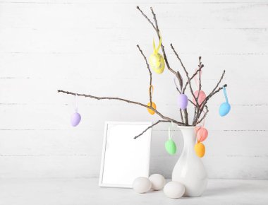 Ağaç dallı vazo, Paskalya yumurtası ve beyaz ahşap arka planda boş fotoğraf çerçevesi.