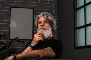 Yakışıklı, olgun sakallı bir adamın portresi. Evdeki koltukta oturuyor.