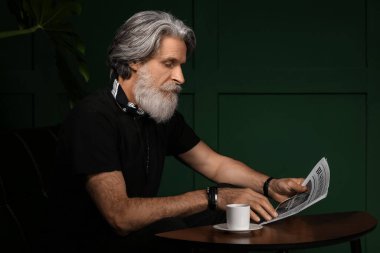 Evde gazete okuyan, olgun sakallı yakışıklı bir adam.