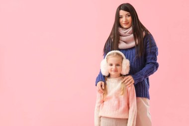 Küçük kız ve annesi pembe arka planda kalın kazaklar giyiyordu.