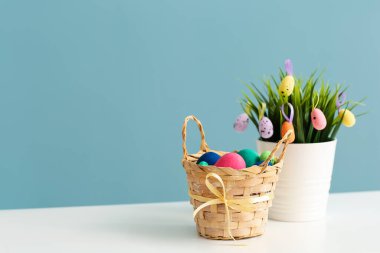Mavi duvarın yanındaki masa üzerinde boyanmış Paskalya yumurtası ve çiçek sepeti.