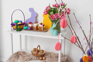 Paskalya pastaları, yumurtalar ve dekorlar beyaz duvarın yanındaki raf ünitesinde.