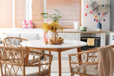 Mimoza çiçekli vazo, Paskalya tavşanı ve mutfak masasında yumurta sepeti.