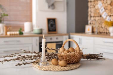 Basket with Easter eggs, pussy willow branches and burning candle on dining table
