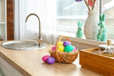 Pencerenin yanındaki ahşap mutfak tezgahında Paskalya yumurtaları olan sepet.