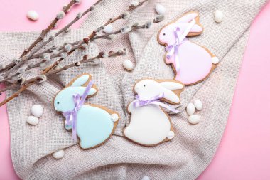 Delicious Easter cookies in shape of bunny, candies and pussy willow branches on pink background