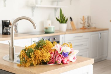 Açık mutfakta bir buket çiçekle lavabo.