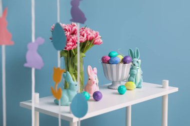 Paskalya yumurtaları, tavşanlar ve renkli duvarların yanında güzel laleler olan raf ünitesi.