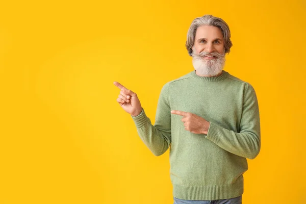 Przystojny Starszy Pan Swetrze Wskazujący Coś Żółtym Tle — Zdjęcie stockowe