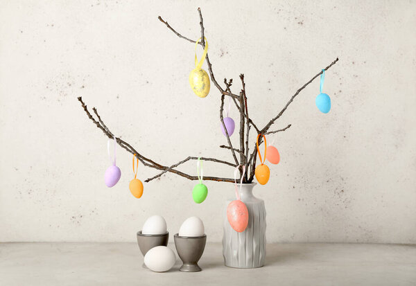 Easter eggs and vase with tree branches on light background