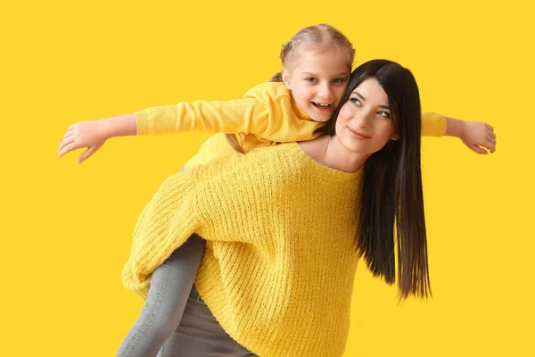 年轻的母亲背着她的小女儿背负着黄色的背景 — 图库照片