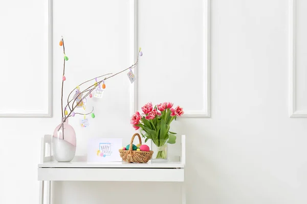 バスケット 塗装卵 花や白い壁の近くのテーブルの上にグリーティングカードを持つ美しいイースター組成 — ストック写真