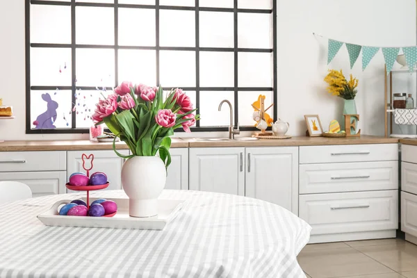 用复活节彩蛋和郁金香花瓶站在时尚厨房的饭桌上 — 图库照片