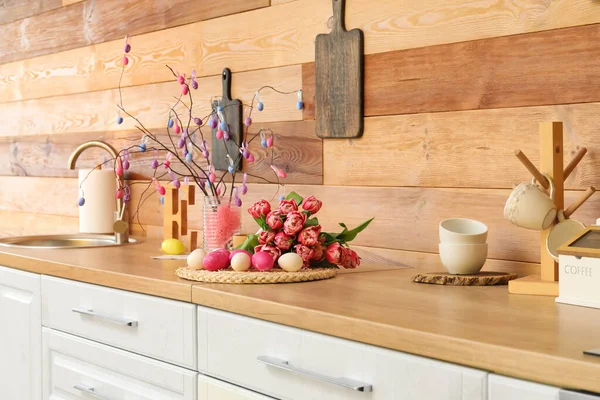 厨房内部木制墙边柜台上的复活节彩蛋和郁金香花束 — 图库照片