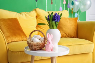 Çiçekler, Paskalya yumurtası sepeti ve rahat kanepenin yanındaki masada tavşan.