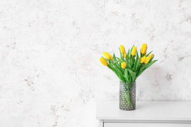 Gür duvarın yanındaki çekmecelerin üstünde güzel laleler olan vazo.