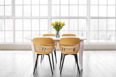 Yemek masasında laleler ve aydınlık odada sandalyeler olan vazo.