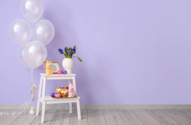 Paskalya pastaları, yumurtalar, çiçekli vazolar ve odanın renk duvarının yanındaki merdiven taburesinde süslü dekorlar.