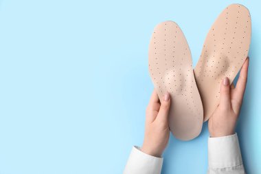 Mavi arka planda bej renkli ortopedik tabanlı kadın elleri