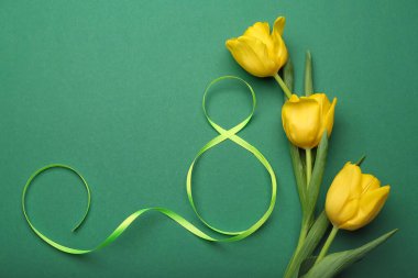 Yeşil arka planda Uluslararası Kadınlar Günü kutlamaları için kurdele ve çiçeklerden oluşan figür 8