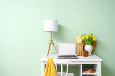 Modern dizüstü bilgisayarı, laleleri ve renk duvarına yakın tebrik kartı olan Paskalya tavşanı olan bir iş yeri.