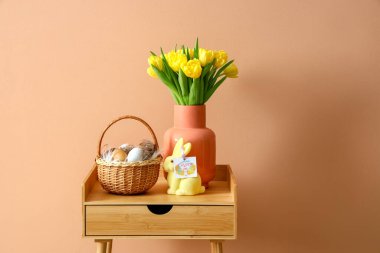 Paskalya yumurtaları, tavşan ve laleler renkli duvarın yanındaki ahşap masada.