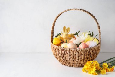 Boyanmış Paskalya yumurtaları, tavşan ve açık arkaplanda çiçekler olan sepet.