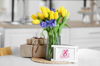 8 Marş yazılı tebrik kartı, yemek masasında çiçekler ve hediye kutuları. Uluslararası Kadınlar Günü kutlamaları