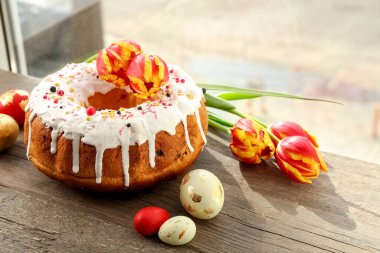 Tahta masadaki yumurtalı ve çiçekli Paskalya pastası.