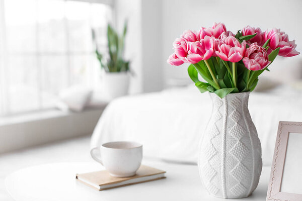 Vase with tulips, book and cup on table in room