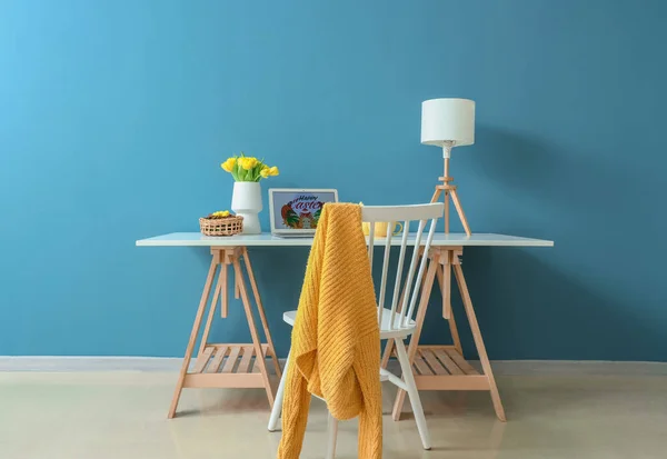 美しいチューリップ イースターエッグ 部屋のインテリアの色の壁の近くのテーブルの上のランプとラップトップ — ストック写真