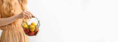 Beyaz zemin üzerinde boyanmış Paskalya yumurtaları olan sepeti tutan bir kadın.