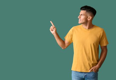 Şık tişörtlü yakışıklı genç adam arka plandaki bir şeyi işaret ediyor.