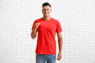 Beyaz tuğla arka planda şık tişörtlü yakışıklı genç adam.
