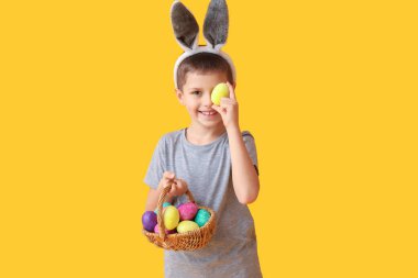 Tavşan kulaklı komik küçük çocuk ve sarı arka planda Paskalya sepeti.