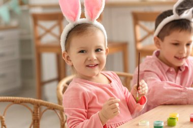 Erkek kardeşiyle birlikte evde paskalya yumurtası boyayan tavşan kulaklı şirin bir kız.