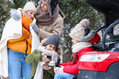 Karlı kış gününde, arabasının yanında sıcak çay içen mutlu bir aile.