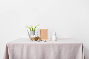 Boş fotoğraf çerçevesi, Paskalya yumurtaları, tavşanlar ve laleler ışık duvarının yanında.