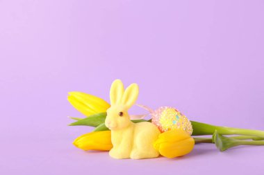 Güzel Paskalya tavşanı, lale çiçekleri ve mor arka planda boyanmış yumurta.